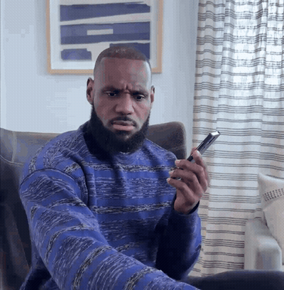 A Man In A Blue Sweater Holds A Cell Phone GIF