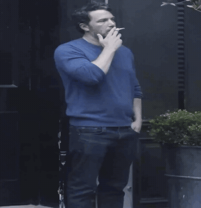 A Man In A Blue Sweater Holds A Cigarette GIF
