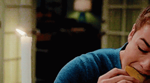 A Man In A Blue Sweater Is Eating A Piece Of Food In Front Of A Lit Candle . GIF