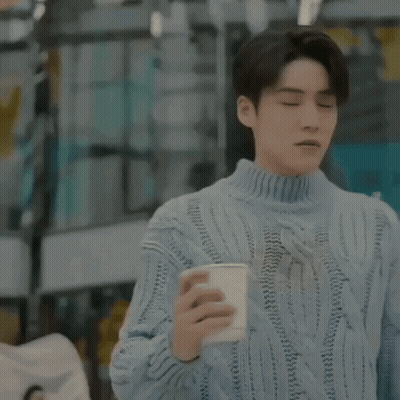 A Man In A Blue Sweater Is Holding A Cup Of Coffee In A Restaurant . GIF