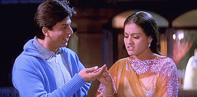 A Man In A Blue Sweater Is Holding A Woman 'S Hand In Front Of Her Face GIF