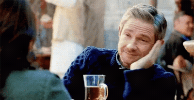 A Man In A Blue Sweater Is Sitting At A Table With A Glass Of Beer In Front Of Him . GIF