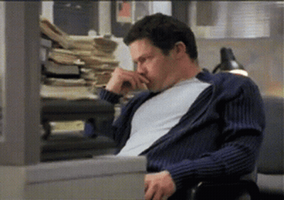 A Man In A Blue Sweater Is Sitting In Front Of A Pile Of Papers GIF