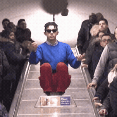 A Man In A Blue Sweater Is Sitting On An Escalator GIF