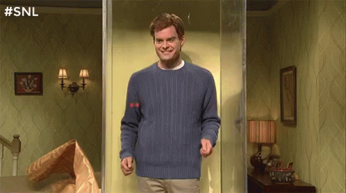 A Man In A Blue Sweater Is Standing In A Room With A Bag Of Food . GIF