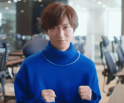 A Man In A Blue Sweater Is Standing In An Office With His Fists Up . GIF