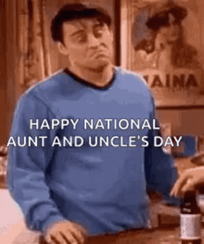 A Man In A Blue Sweater Is Standing In Front Of A Counter And A Bottle Of Wine . GIF