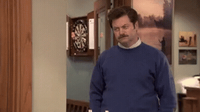 A Man In A Blue Sweater Is Standing In Front Of A Dartboard GIF