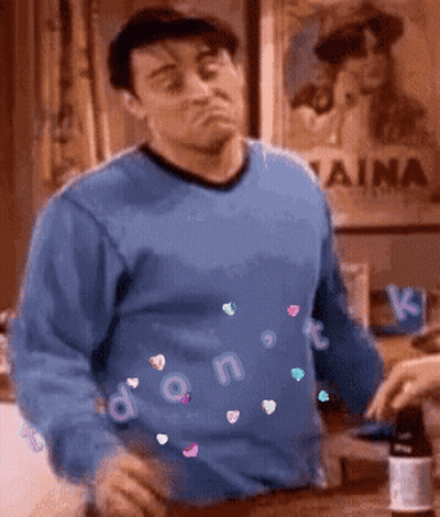 A Man In A Blue Sweater Is Standing In Front Of A Sign That Says Naina GIF
