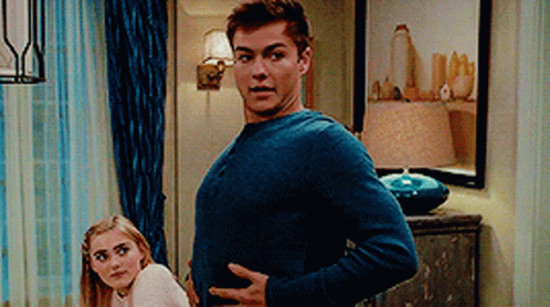 A Man In A Blue Sweater Is Standing Next To A Woman In A White Sweater . GIF