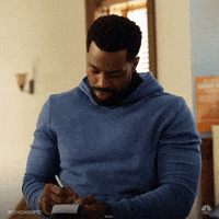 A Man In A Blue Sweater Is Writing In A Notebook GIF