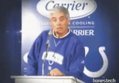 A Man In A Blue Sweater Stands At A Podium In Front Of A Carrier Logo GIF