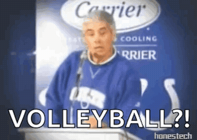 A Man In A Blue Sweater Stands At A Podium With The Words " Volleyball " Written On It GIF
