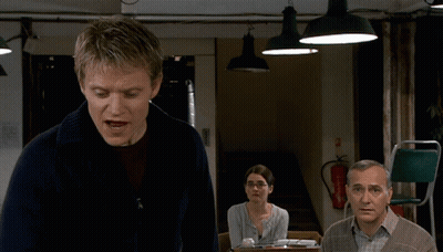 A Man In A Blue Sweater Stands In Front Of A Fire Extinguisher GIF
