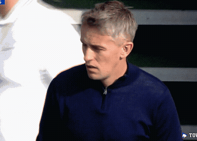 A Man In A Blue Sweater Stands In Front Of A Tov Sign GIF