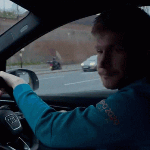 A Man In A Blue Sweater With The Word Peace On It Is Driving An Audi GIF