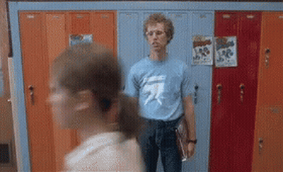 A Man In A Blue T-Shirt Is Standing In Front Of A Row Of Lockers . GIF