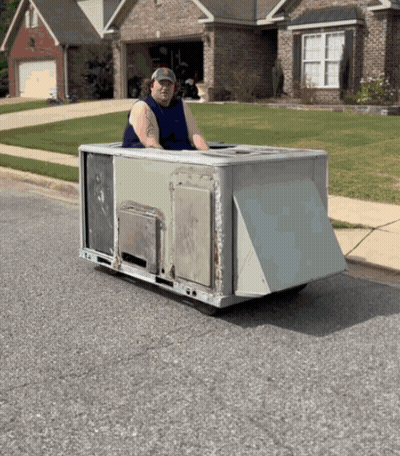 A Man In A Blue Tank Top Is Driving A Small Vehicle On The Street GIF