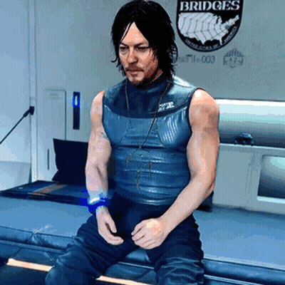 A Man In A Blue Tank Top Is Sitting In Front Of A Wall That Says Bridges GIF