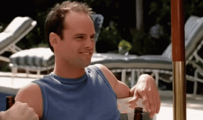 A Man In A Blue Tank Top Is Sitting Under An Umbrella With A Bottle Of Beer . GIF