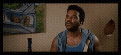 A Man In A Blue Tank Top Is Standing In Front Of A Painting On A Wall GIF