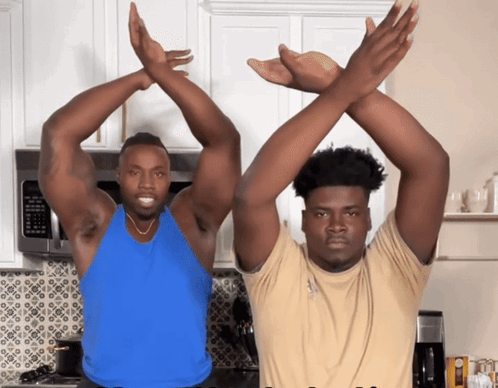 A Man In A Blue Tank Top Stands Next To A Man In A Tan Shirt GIF