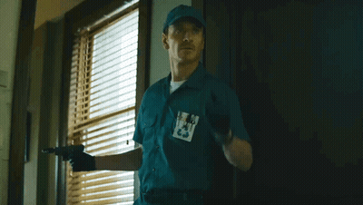A Man In A Blue Uniform Holds A Gun In Front Of A Window With Blinds .. GIF