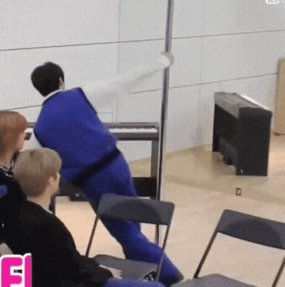 A Man In A Blue Vest Is Leaning Against A Pole GIF