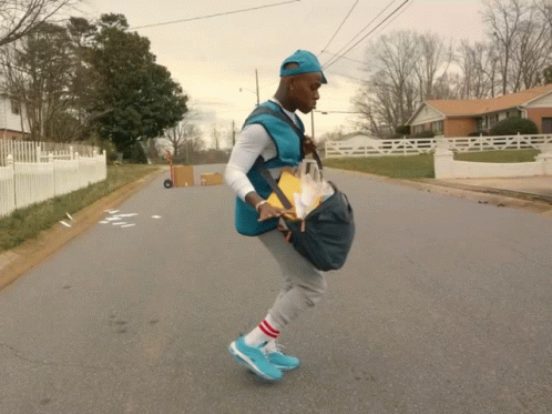 A Man In A Blue Vest Is Walking Down A Street With A Bag On His Back GIF