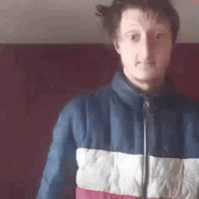 a man in a blue , white , and red jacket is standing in front of a red wall .