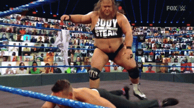 A Man In A Body Of A Steak Shirt Is Standing Over Another Man In A Wrestling Ring GIF