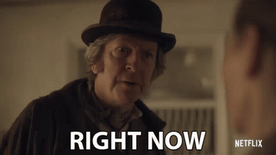 A Man In A Bowler Hat Is Talking To Another Man And Says Right Now . GIF
