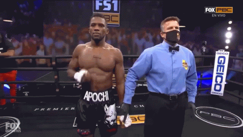 A Man In A Boxing Ring With Apochi On His Shorts Is Being Congratulated By A Referee GIF