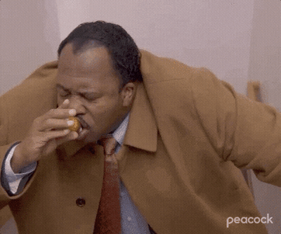 A Man In A Brown Coat And Tie Is Eating A Donut . GIF