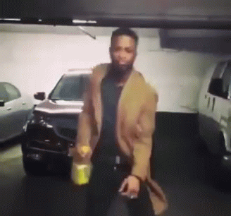 A Man In A Brown Coat Is Standing In Front Of A Car In A Parking Garage GIF