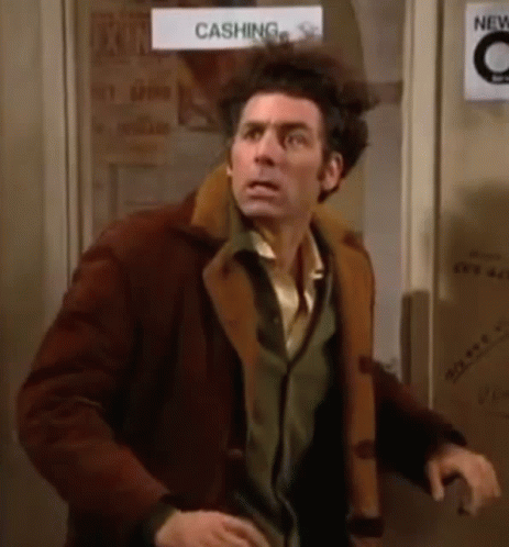 A Man In A Brown Coat Is Standing In Front Of A Door With A Sign On It That Says Cashing . GIF