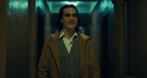 A Man In A Brown Coat Stands In A Hallway GIF