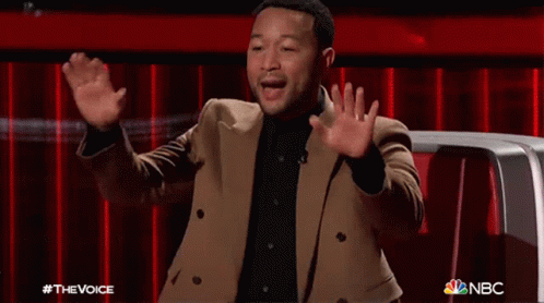 A Man In A Brown Jacket Is Sitting In Front Of A Red Curtain With His Hands In The Air .. GIF