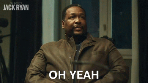 A Man In A Brown Jacket Is Sitting In Front Of A Sign That Says " Oh Yeah " GIF