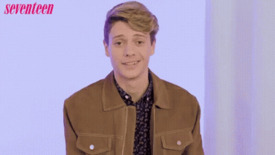 A Man In A Brown Jacket Is Smiling In Front Of A Seventeen Ad GIF