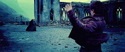 A Man In A Brown Jacket Is Standing In Front Of A Ruined Building With His Hands In The Air GIF