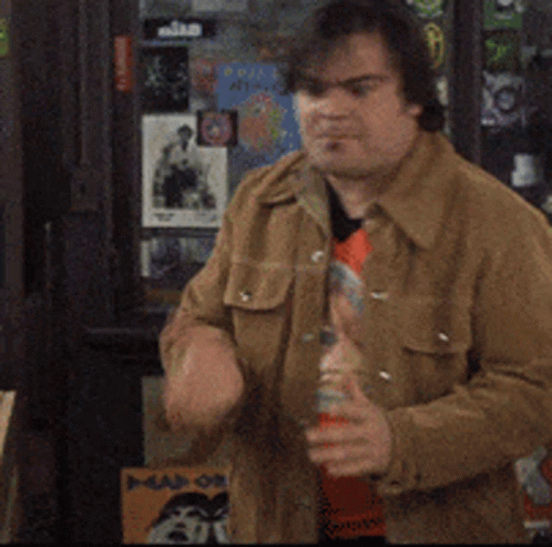 A Man In A Brown Jacket Is Standing In Front Of A Wall With Stickers On It Including One That Says ' Nike ' GIF