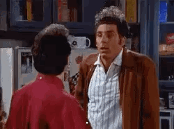 A Man In A Brown Jacket Is Talking To Another Man In A Red Shirt In A Kitchen . GIF