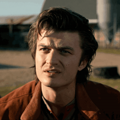 A Man In A Brown Jacket Looks At The Camera GIF