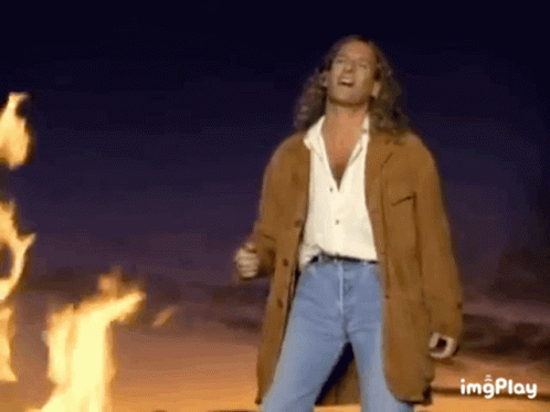 Man In Brown Jacket In Front Of Fire GIF