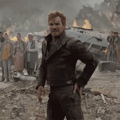 a man in a brown leather jacket stands in front of a burning building