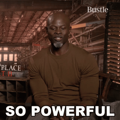 A Man In A Brown Shirt Is Sitting In Front Of A Poster That Says " So Powerful " GIF