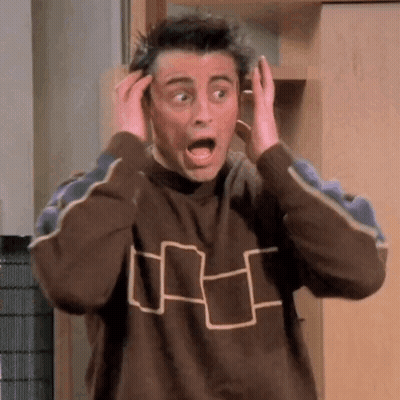 A Man In A Brown Sweater Is Making A Surprised Face While Holding His Hands To His Head . GIF