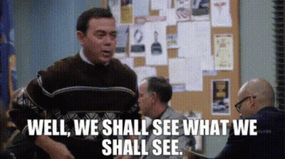 A Man In A Brown Sweater Is Standing In Front Of A Bulletin Board And Says Well We Shall See What We Shall See GIF