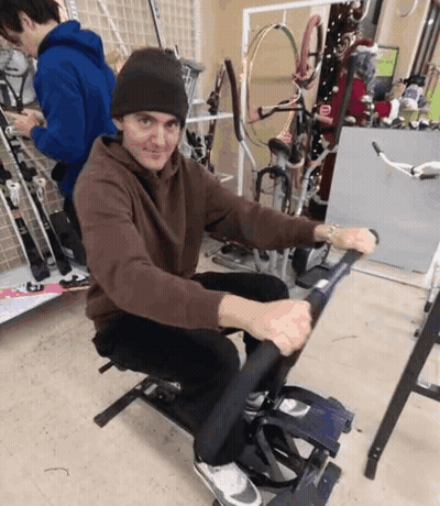 A Man In A Brown Sweatshirt Is Sitting On A Machine GIF
